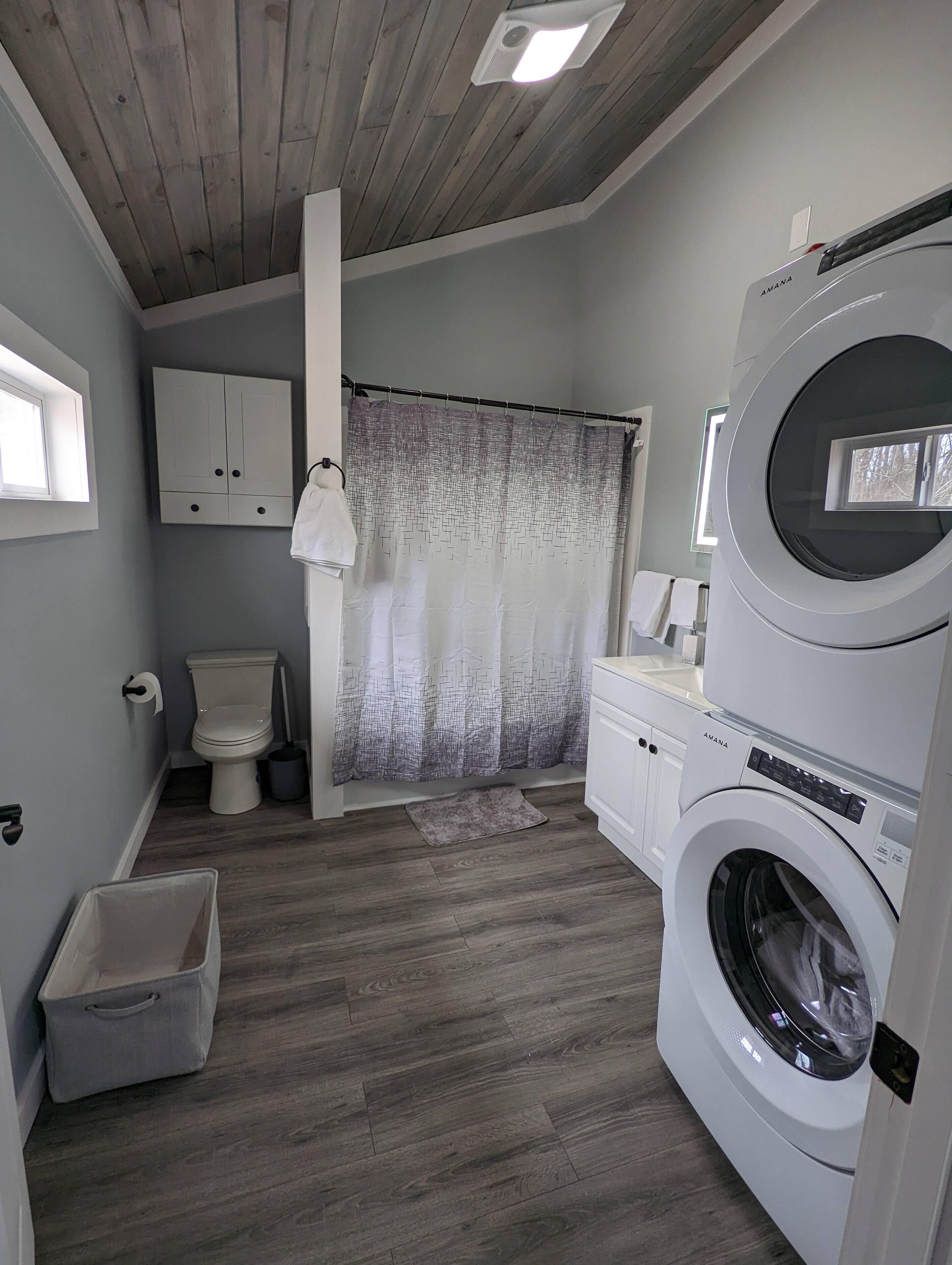 A laundry room with a washing machine, a toilet, and a shower curtain.