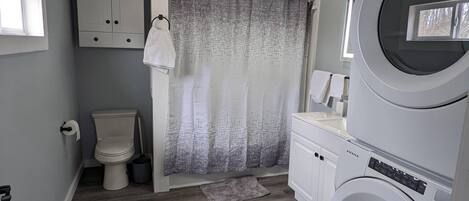 A laundry room with a washing machine, a toilet, and a shower curtain.
