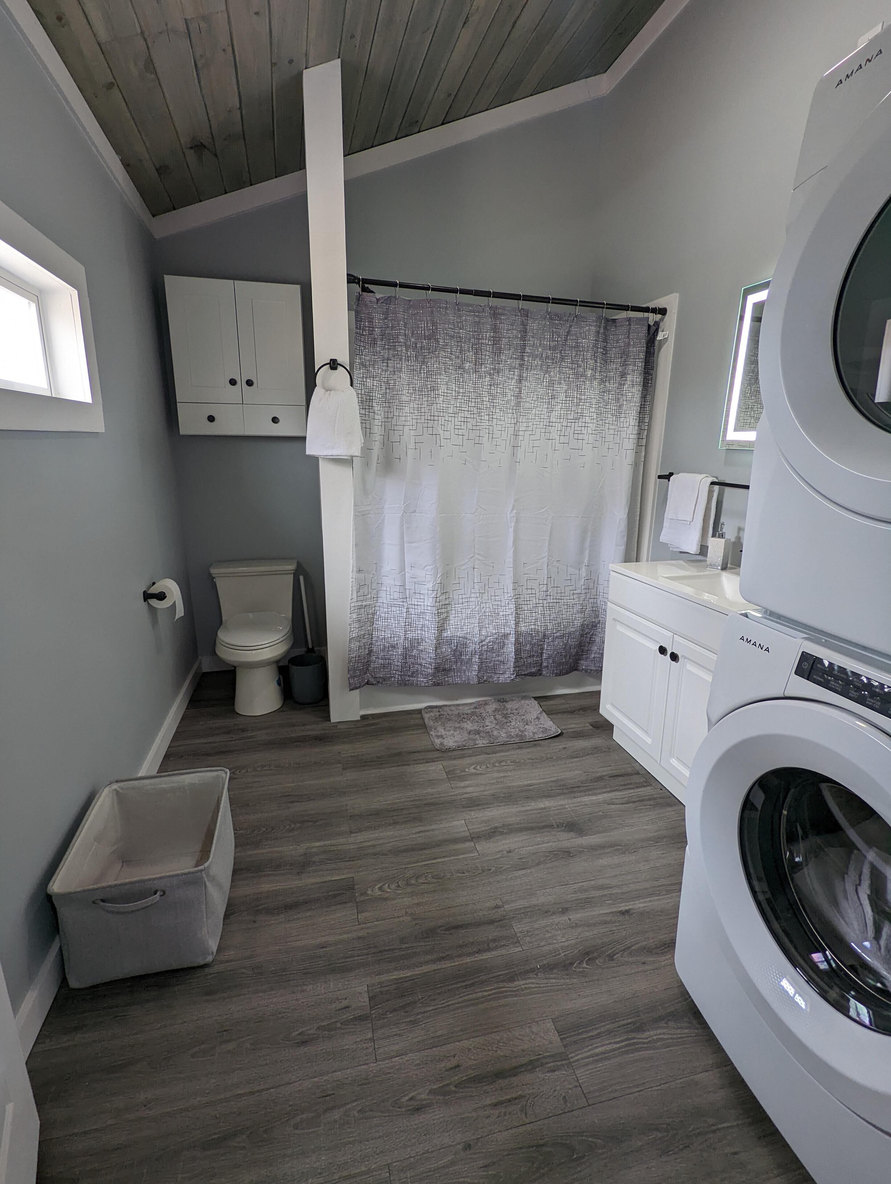 Une petite salle de bain comprenant des toilettes, un rideau de douche, un lave-linge et un meuble de rangement.