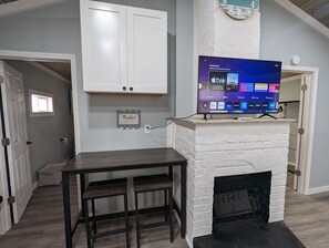 A living room with a white brick fireplace, a flat-screen TV mounted above it, and a small table with two chairs.