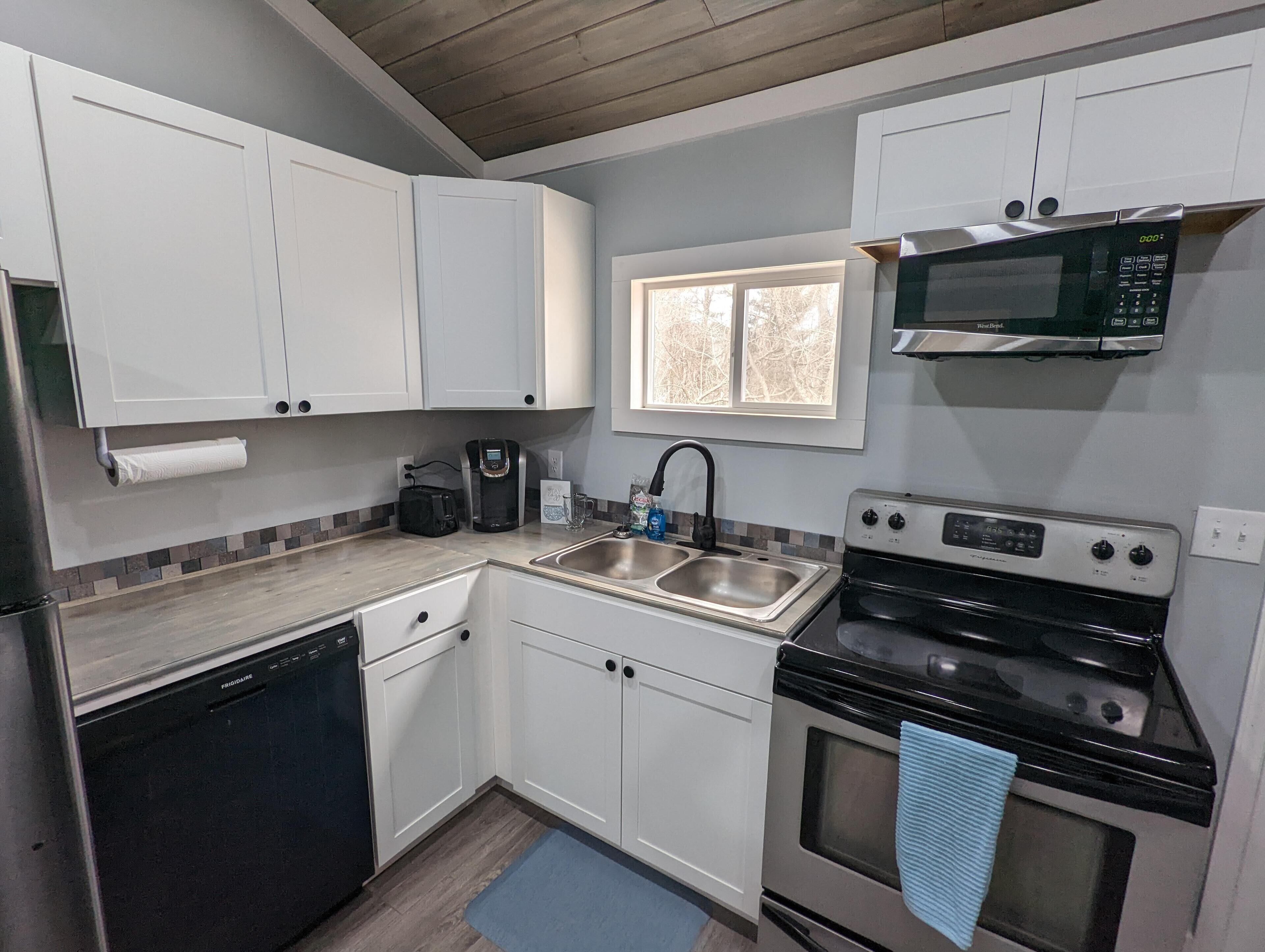 A compact kitchen with white cabinets, a stainless steel sink, a coffee maker, a microwave, and a stove.