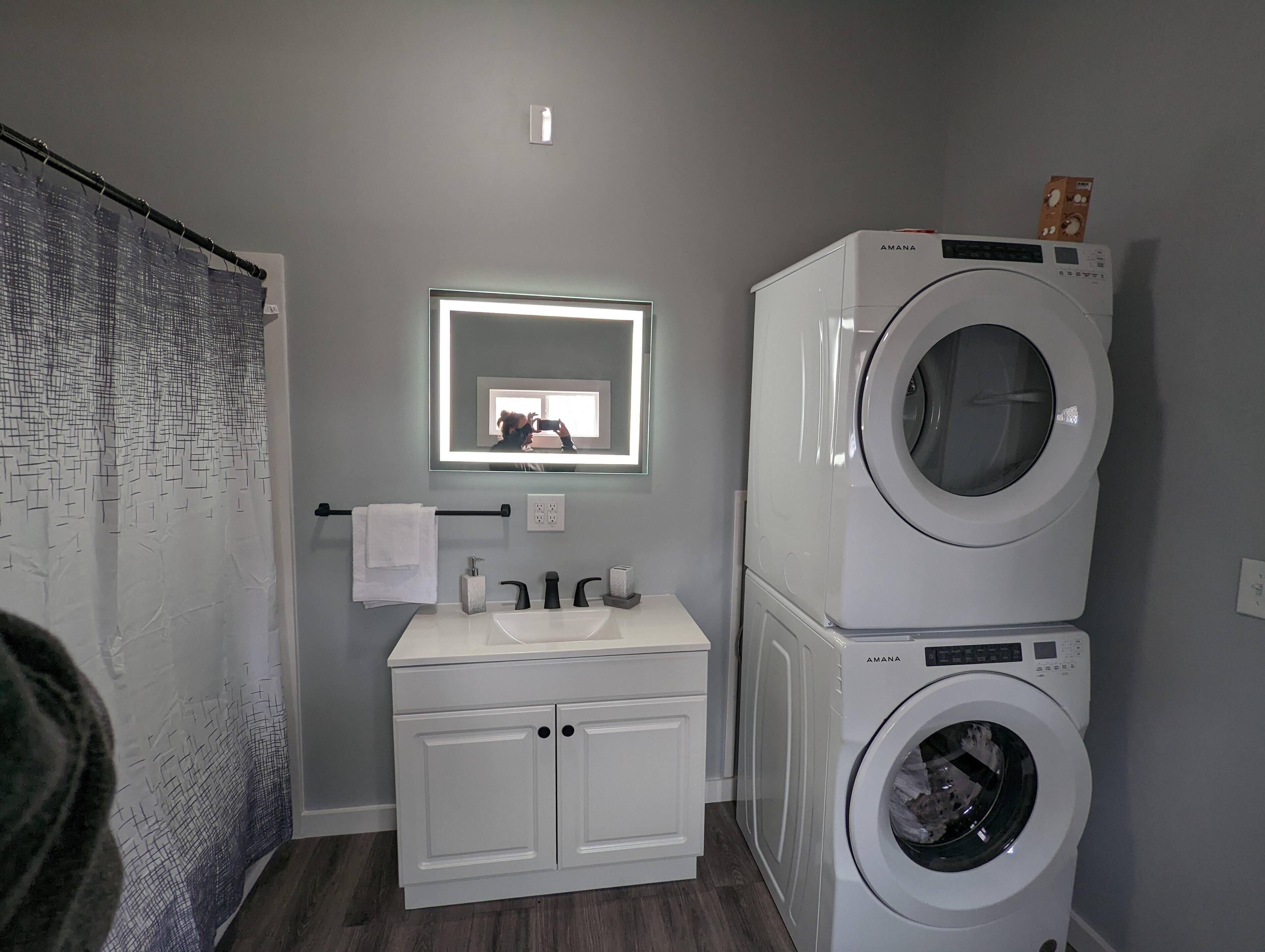 A compact bathroom with a white sink, a mirror, and a stacked washer and dryer unit.