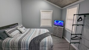 Un dormitorio con cama, televisión, cómoda y perchero.