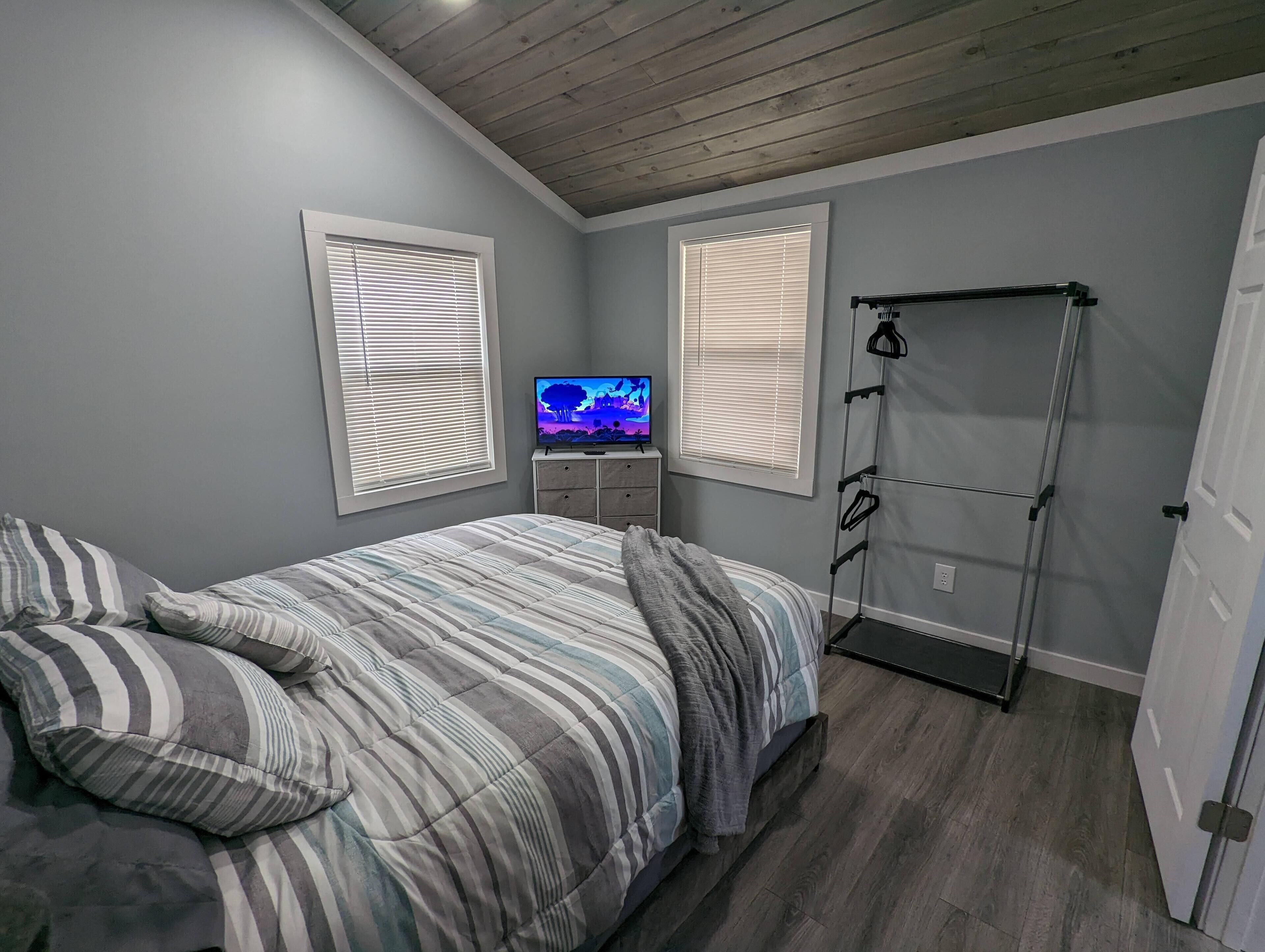 Quarto com cama, televisão em um suporte e um cabideiro.
