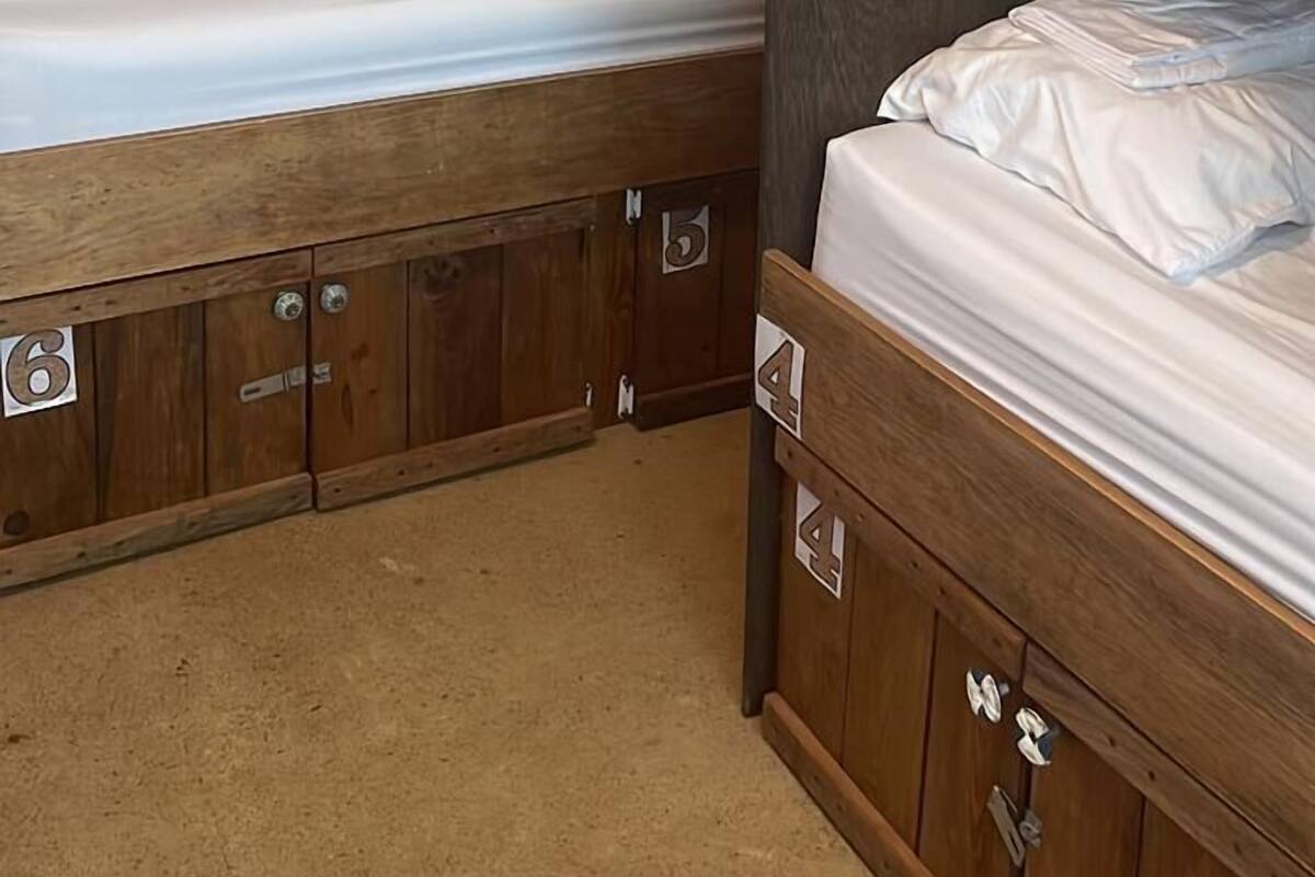Quarto com beliches de madeira, compartimentos numerados e cortinas vermelhas.