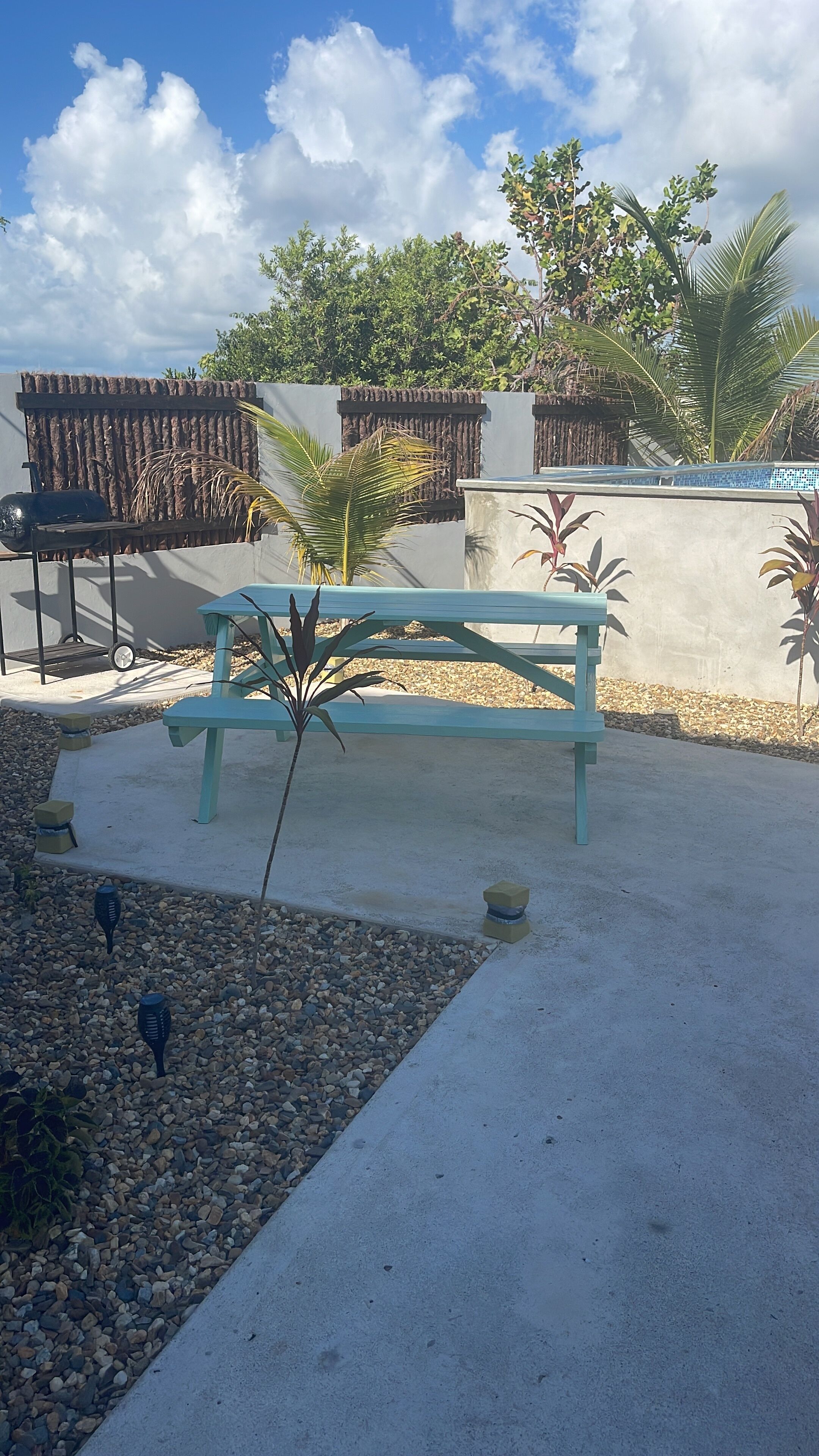 A patio area with a light blue bench, a small plant, and a decorative wall.
