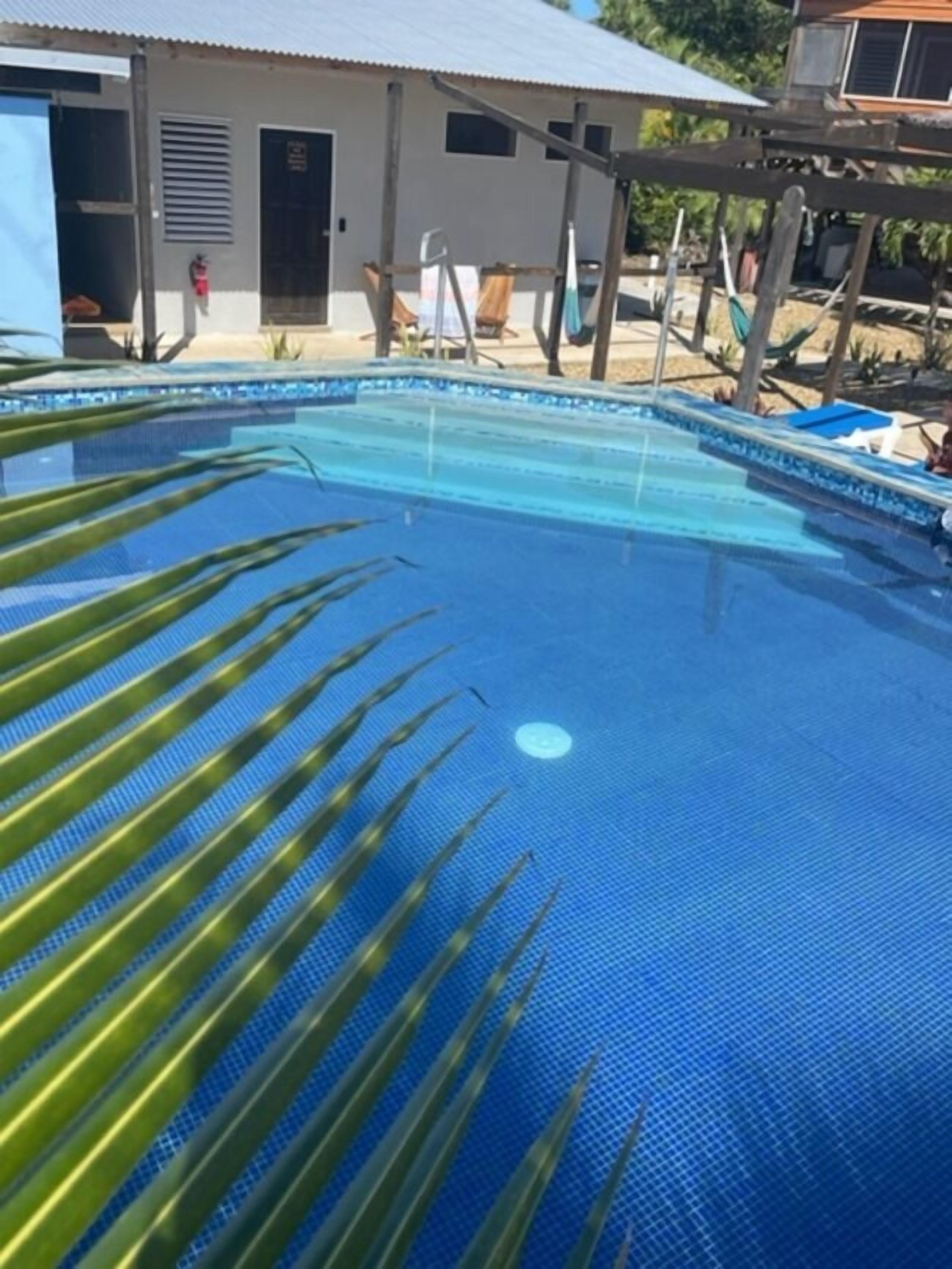 Una piscina con pavimento piastrellato blu, circondata da un edificio semplice con tetto in metallo e una porta.