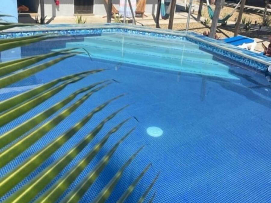 Una piscina con pavimento piastrellato blu, circondata da un edificio semplice con tetto in metallo e una porta.