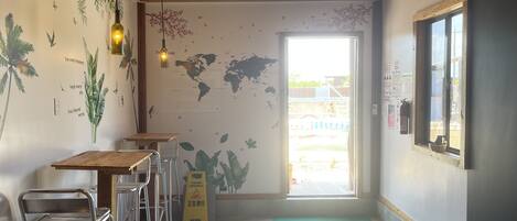 A cafe interior with a wooden ceiling, world map wall art, a 'WELCOME' mat, and a 'CLEANING INPROGRESS' sign.