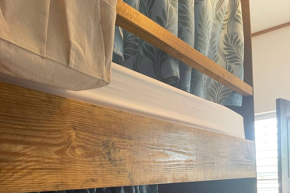Uma cama beliche com estrutura de madeira, cortinas azuis estampadas e colchão branco.