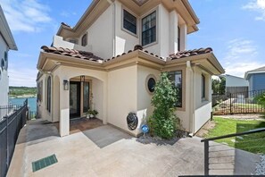 A two-story house with a covered patio, a small tree, and a visible driveway.
