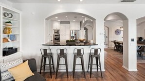 A modern kitchen with white cabinets, a central island with bar stools, and an open-plan layout connecting to a dining area.