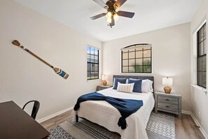 A bedroom with a bed, a ceiling fan, a window, and a wall-mounted wooden paddle.