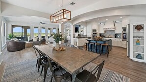 A spacious kitchen with a central island, a dining area with a wooden table, and a large open living space with a view.