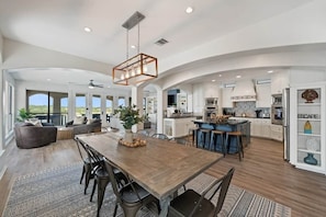A spacious kitchen with a central island, a dining area with a wooden table, and a large open living space with a view.