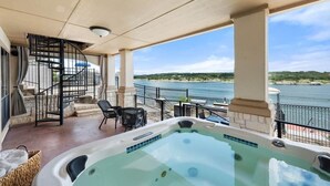 A hot tub on a balcony with a view of the water, a staircase, and outdoor furniture.