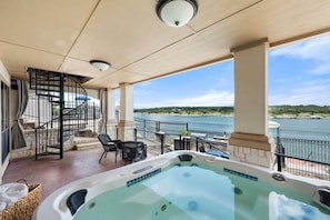 A hot tub on a balcony with a view of the water, a staircase, and outdoor furniture.