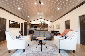 Un'ampia zona giorno con soffitto alto, un'area salotto centrale e una cucina sullo sfondo.