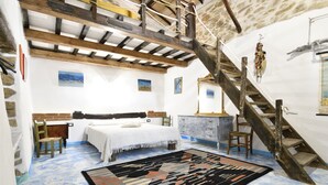 A bedroom with a bed, wooden chair, desk, and a staircase. - The pergola (old house) inside the history of Sardinia. (Gergei)