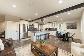 A spacious kitchen with a central island, stainless steel appliances, and a dining area with bar stools. - WATERFRONT Unique Hangar Home Runway Pilot Paradise Jacuzzi-Aurora View (Fairbanks)