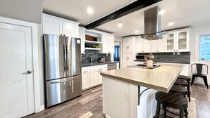Una cocina moderna con armarios blancos, electrodomésticos de acero inoxidable y una isla central con taburetes de bar.