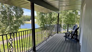 Una terraza de madera con baranda metálica, con vista a un lago y árboles.
