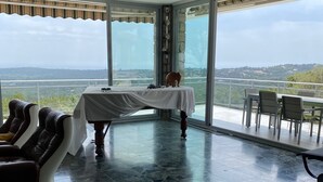 Ein geräumiges Zimmer mit einem großen Tisch, einem Massagesessel und Blick auf eine weite Landschaft durch große Fenster.