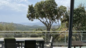 Eine Terrasse mit Tisch und Stühlen, eine Glastür und Blick auf Baum und Landschaft.