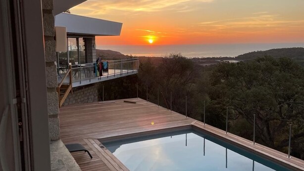 Ein moderner Außenpool mit Holzterrasse und Steinmauer, mit Blick auf eine malerische Landschaft und Sonnenuntergang.