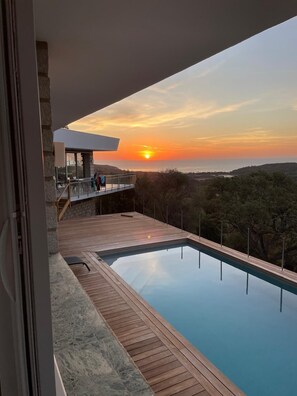 A modern outdoor swimming pool with a wooden deck and a stone wall, overlooking a scenic landscape with a sunset view. - Villa 8 pers with panoramic view on gulf of porto vecchio, 5 min beaches (SAINTE LUCIE DE PORTO VECCHIO)