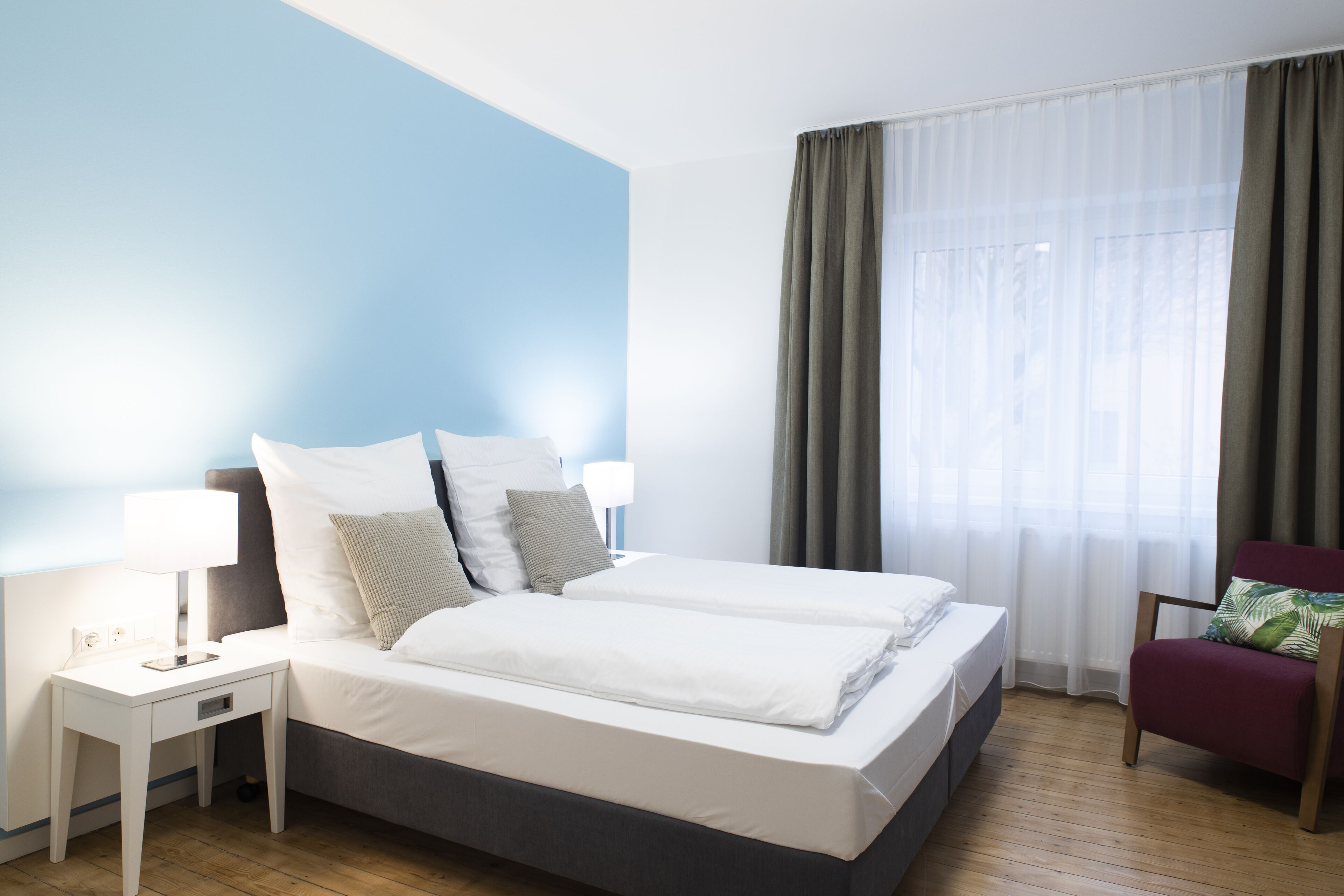 Une chambre d’hôtel avec un lit, des tables de chevet, une chaise et une fenêtre avec des rideaux.