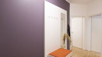 A hallway with a purple wall, a white door, and a small table with an orange cushion.