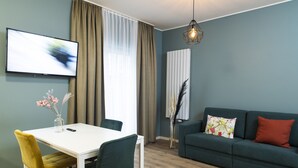 A modern living room with a white dining table, green chairs, a dark green sofa, and a TV mounted on the wall. - Villa am Bahnhof (Fulda)