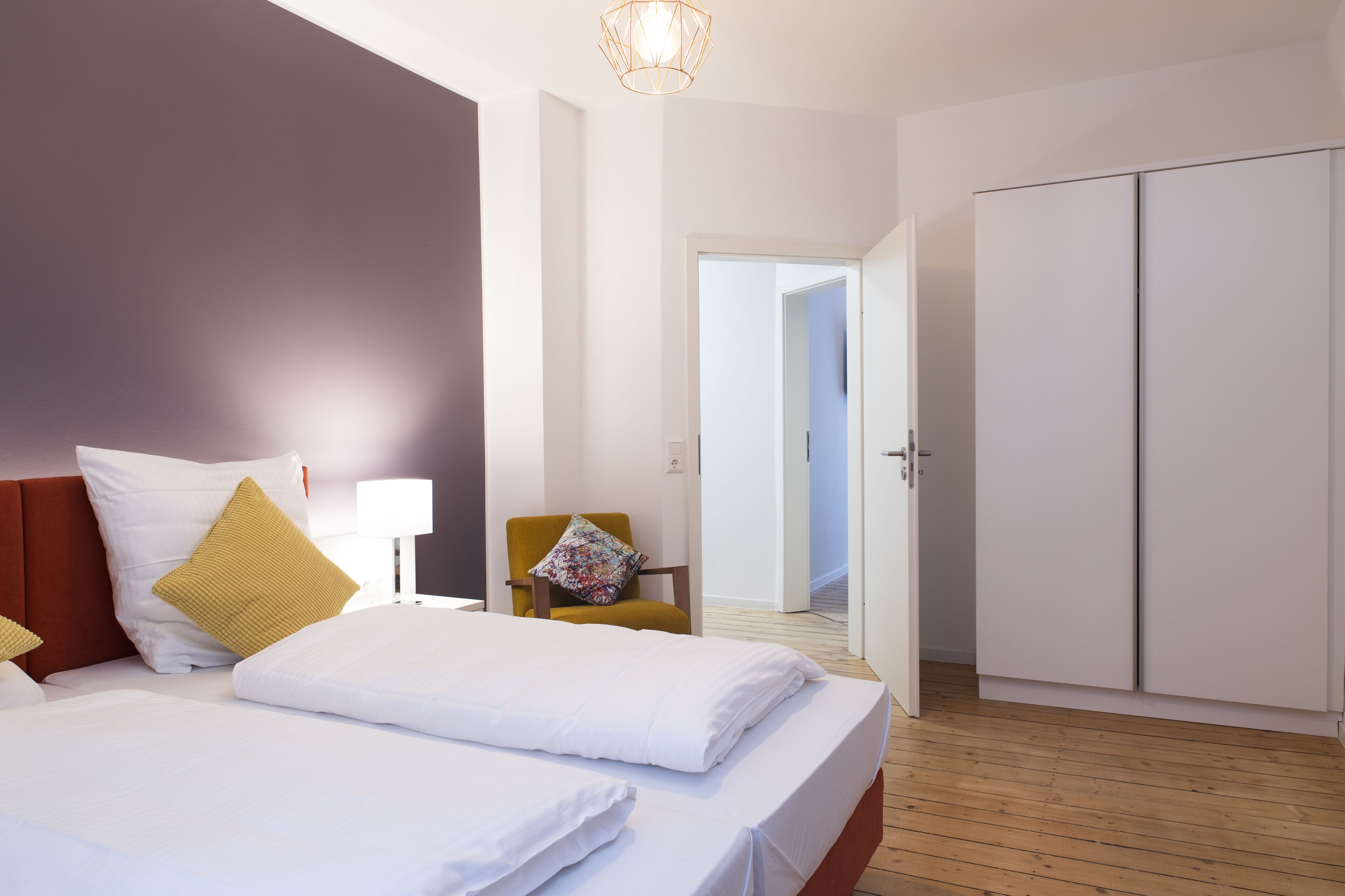 A hotel room with a bed, a chair, a wardrobe, and a door leading to another room.