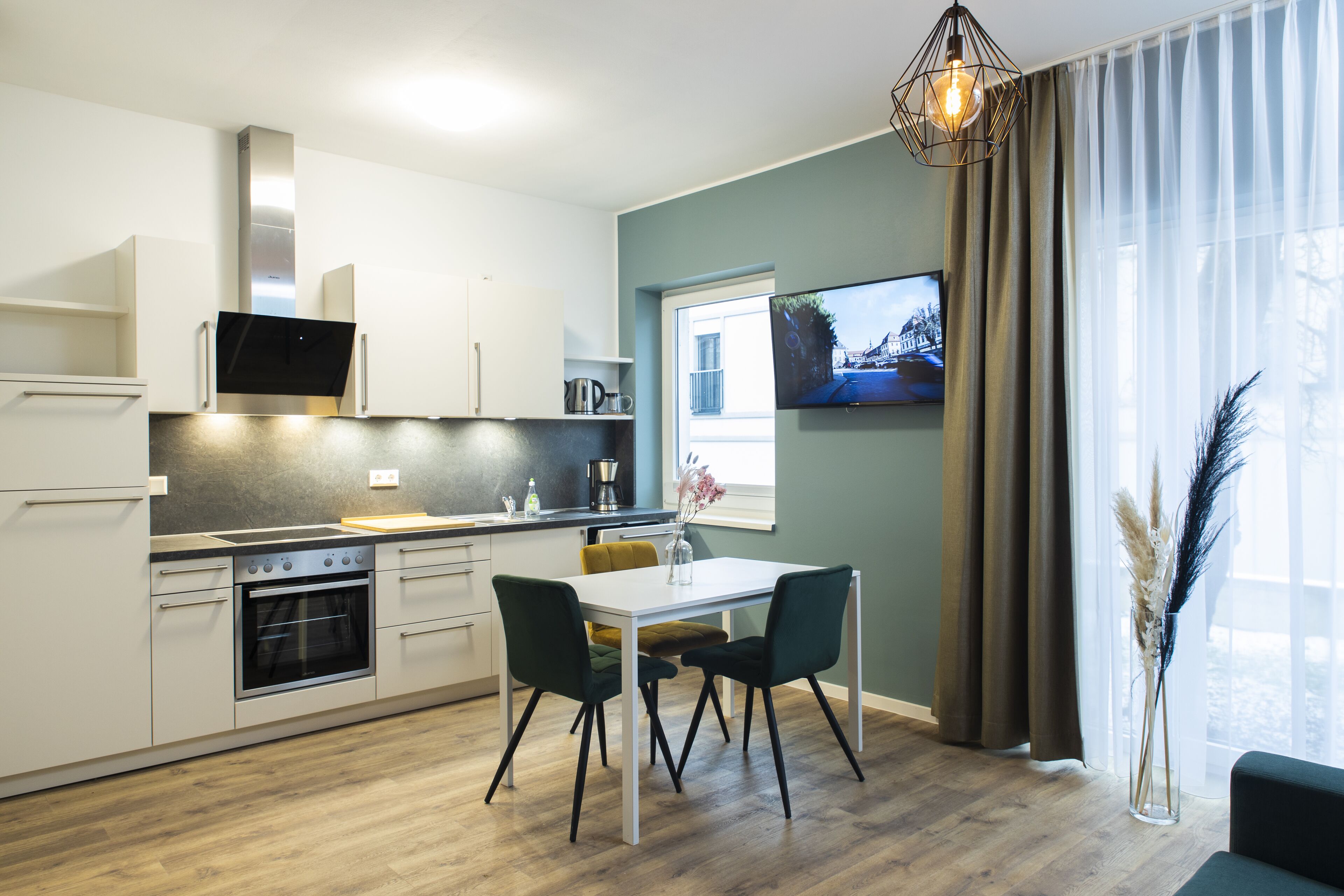 A modern kitchen with white cabinets, a built-in oven, and a dining area with a white table and two chairs.
