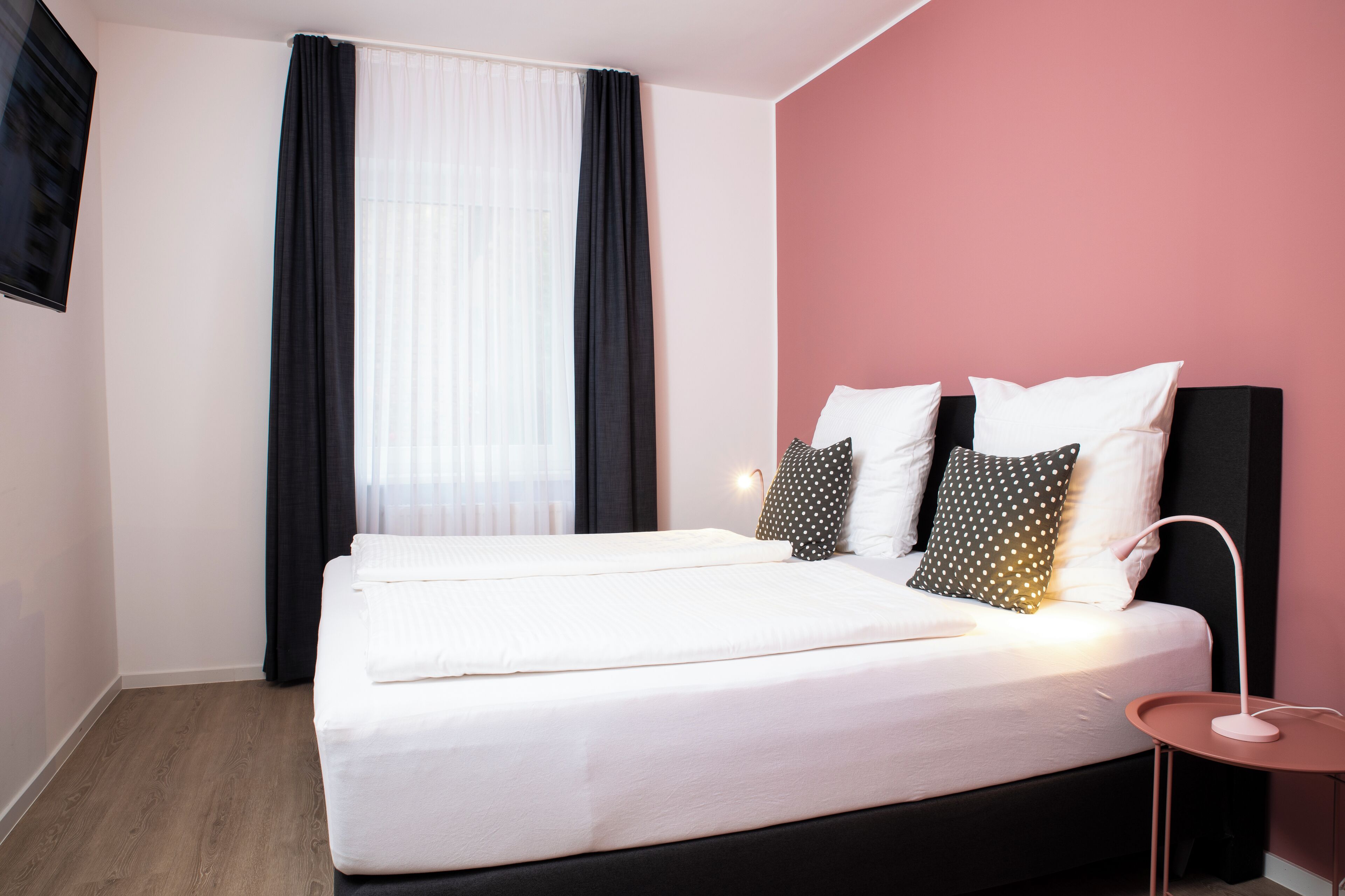 A hotel room with a large bed, a bedside table with a lamp, and a window with curtains.