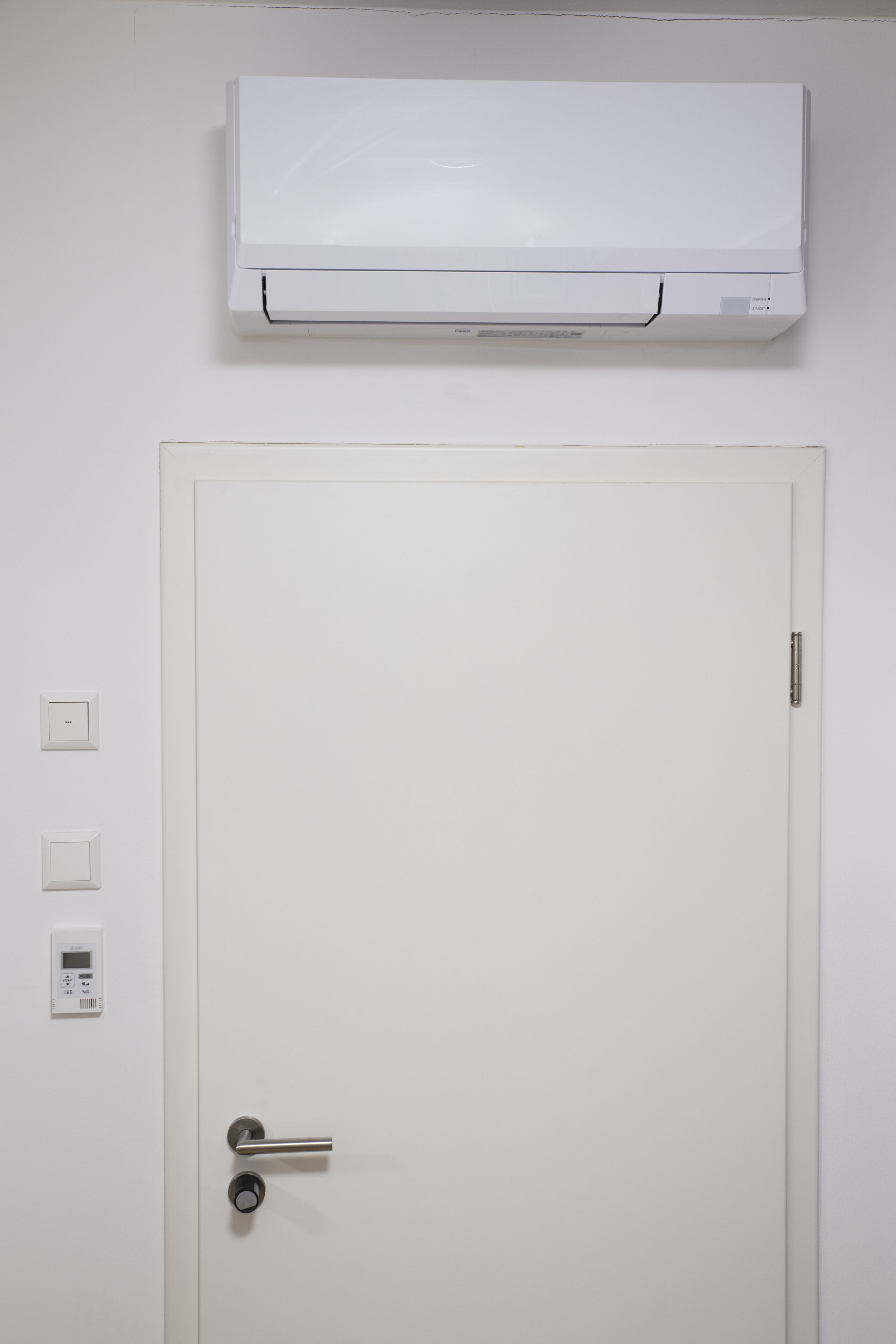 Una puerta blanca con picaporte, un aire acondicionado instalado en la pared y dos interruptores.