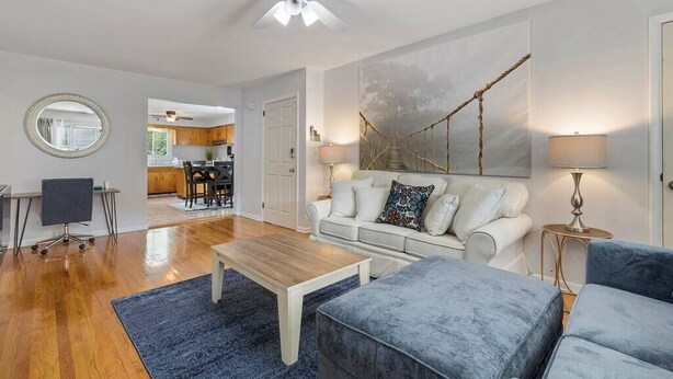 A modern living room with a white sofa, a blue armchair, a wooden coffee table, and a ceiling fan. - The Lennox Stay - Close to NYC ☆ Free Parking (Bloomfield)