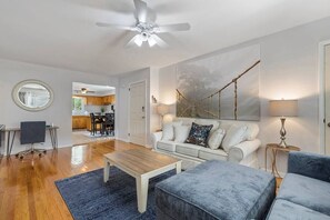 Un salon moderne avec un canapé blanc, un fauteuil bleu, une table basse en bois et un ventilateur de plafond.