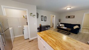 Una cocina moderna con encimera de madera, una zona de comedor con sofá oscuro y un salón con sofá azul.