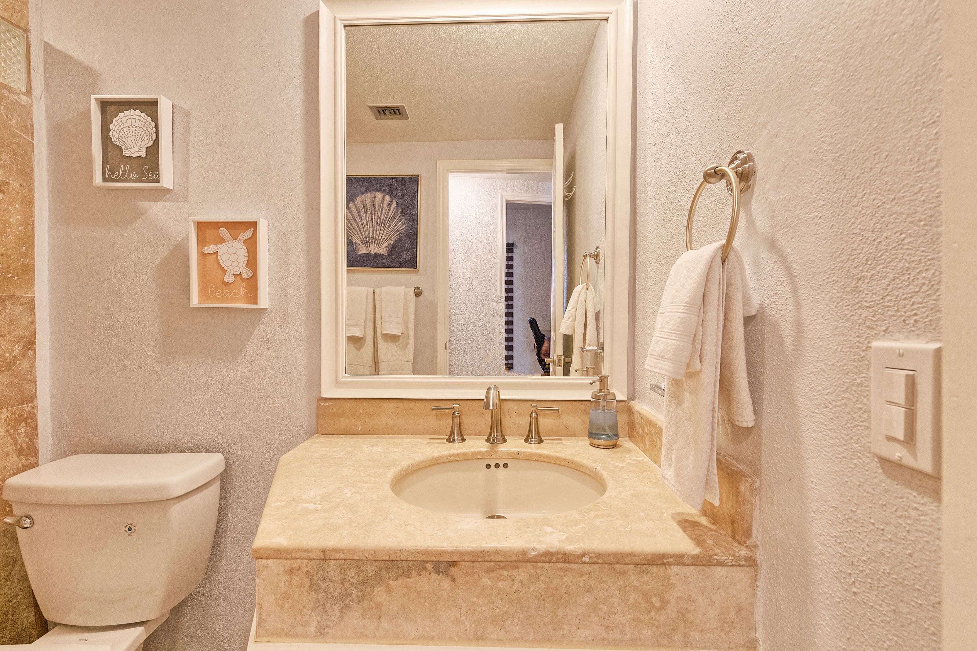 A bathroom with a toilet, sink, and mirror. There are framed pictures on the wall.