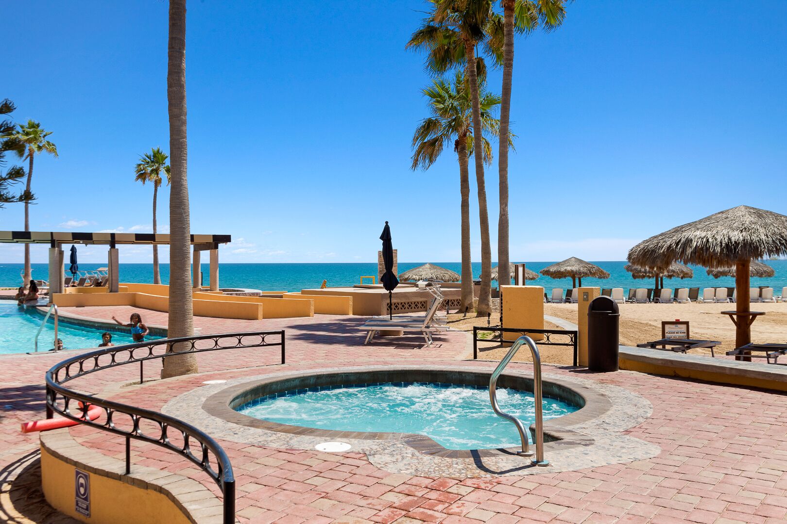 Un espace piscine doté d’un jacuzzi, de chaises longues et de palmiers.