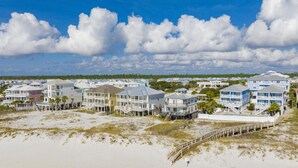 Una zona residenziale sulla spiaggia, con case su palafitte, una passerella in legno e cielo sereno.
