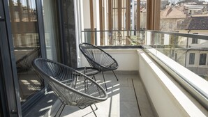 Ein Balkon mit zwei schwarzen Stuhlen aus Draht, einer Glastür und Blick auf Gebäude.