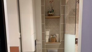 Un baño moderno con inodoro, cabina de ducha de vidrio, toallero con toallas y un escobillón de baño.