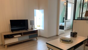 Una sala de estar moderna con un televisor de pantalla plana sobre un mueble de madera, una mesa de centro de vidrio y un espejo que refleja la habitación.