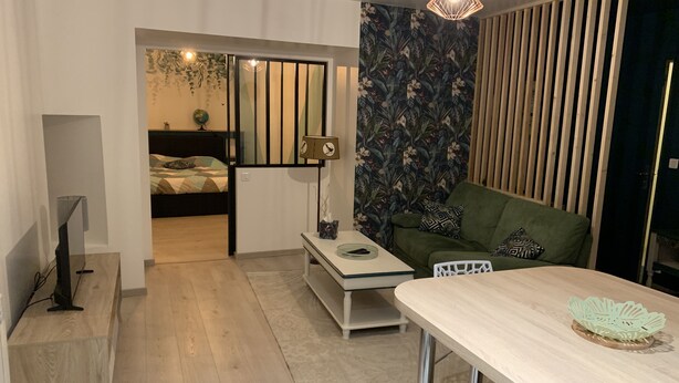 Un espacio habitable moderno con piso de madera, un sofá verde, una mesa blanca y una pared decorativa con motivos florales.