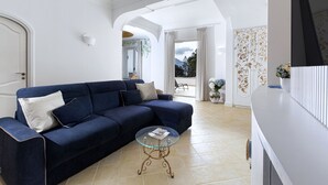 A living room with a blue sofa, a glass coffee table, and a white wall. - Estate4home - Casa Nonna Mary (Positano)
