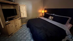 Un dormitorio con una cama, un armario de madera, una televisión y una mesita de noche con una lámpara.