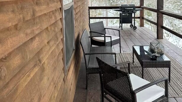 Una terraza de madera con un letrero que dice 'WELCOME TO OUR CAMP', muebles de exterior y vistas a árboles.